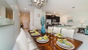 A dining area with a wooden table set for six, white upholstered chairs, and a blue vase centerpiece. - DOG9041 (Davenport)