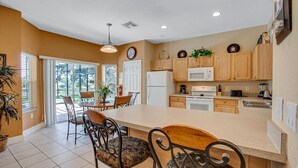 A kitchen with wooden cabinets, a white refrigerator, a stove, and a microwave. There is a dining area with a table and chairs. - DB2605 Windsor Hills Resort Vacation Home (Kissimmee)