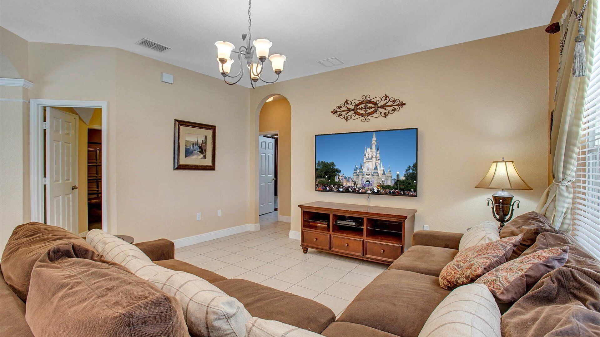 A living room with a large flat-screen TV, a chandelier, a lamp, and a sofa set.