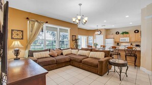 A living room with a sectional sofa, a dining table with chairs, a kitchen area with cabinets and appliances, and a chandelier. - DB2605 Windsor Hills Resort Vacation Home (Kissimmee)