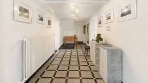 A hallway with a checkered floor, framed pictures on the walls, a radiator, a bench, and a plant on a counter.
