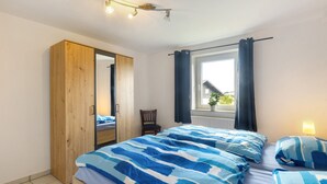 A bedroom with a bed, a wardrobe, a chair, a window with curtains, and a lamp.