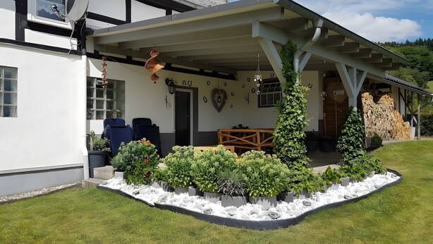 A house with a covered porch, a satellite dish, and a garden with various plants.