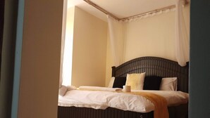 A neatly made bed with white linens and a brown throw blanket, a dark headboard, and a white curtain partially drawn at the window. - The colored house 3 bedroom apartment (Athiriver)
