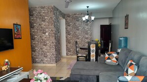 A living room with a sectional sofa, a coffee table, a TV, a fireplace, and a dining area with chairs and a table. - The colored house 3 bedroom apartment (Athiriver)