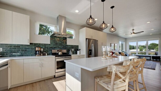 Una cocina moderna con una isla grande, electrodomésticos de acero inoxidable y un salpicadero con azulejos verdes.