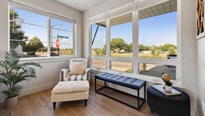 Una habitación con ventanas amplias, un sillón a rayas, un banco y una pequeña mesa con un globo terráqueo.