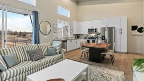 Une cuisine moderne avec des meubles blancs, un réfrigérateur en acier inoxydable et un coin repas comprenant une table et des chaises en bois.