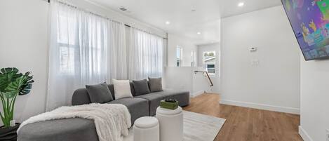 A modern living room with a grey sectional sofa, a white rug, and a green plant.