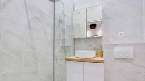 Une salle de bain moderne avec une douche à parois de verre, un lavabo blanc et un plan de toilette en bois.