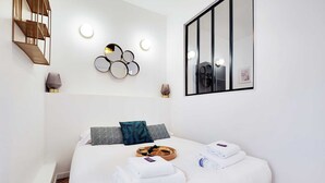Une chambre d’hôtel avec un lit, un miroir fixé au mur, un luminaire décoratif et une petite table sur laquelle se trouve un plateau avec des articles pour le petit-déjeuner.