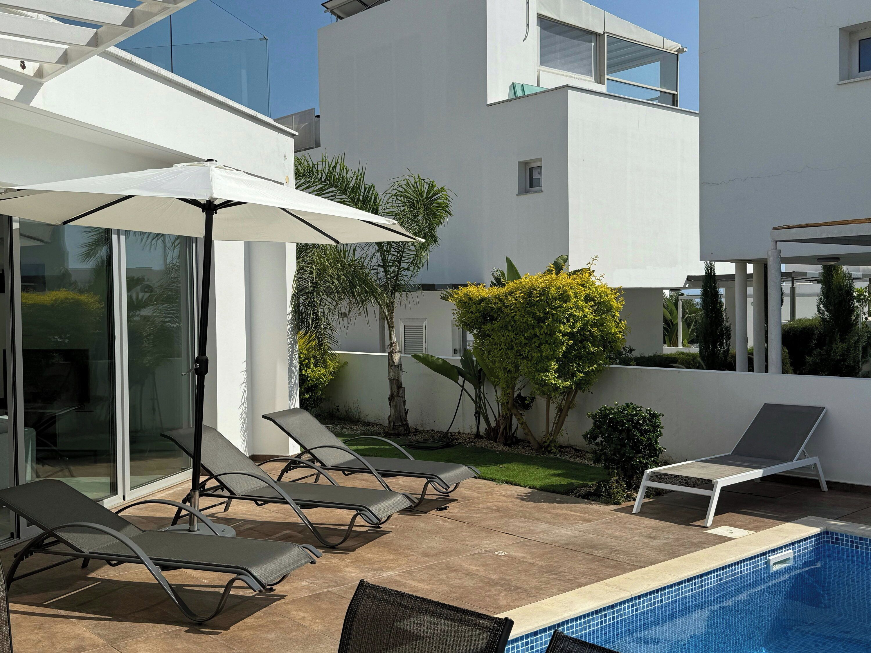 A modern outdoor pool area with lounge chairs, a covered seating area, and a clear view of the surrounding architecture.