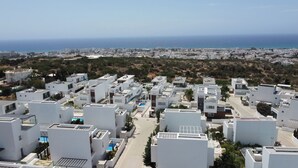 A residential area with modern white buildings, a clear view of the sea, and a distant cityscape.