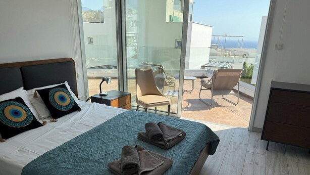 A hotel room with a bed, a desk with a lamp, a chair, and a view of the outside.