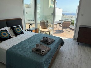 A hotel room with a bed, a desk with a lamp, a chair, and a view of the outside.