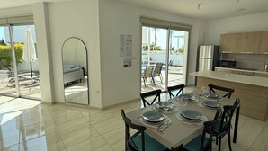 A modern kitchen with a dining area, large windows, and a view of an outdoor pool.