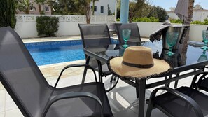 A poolside table with chairs, a woven hat, and glassware.