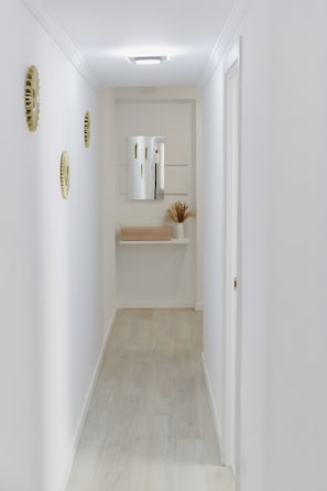 A narrow hallway with white walls, a wooden floor, and a white door at the end.
