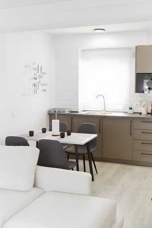 A modern kitchen with a dining area, featuring a white table, chairs, and a sofa.