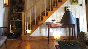 Un escalier en bois avec une rampe, un tableau représentant une grange rouge et une bibliothèque contenant divers objets.