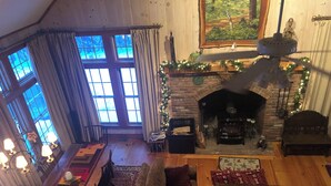 Un salon chaleureux avec une cheminée, des meubles en bois et une grande fenêtre agrémentée de rideaux.