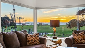 Een kamer met een groot raam dat uitzicht biedt op een zonsondergang boven een golfbaan.