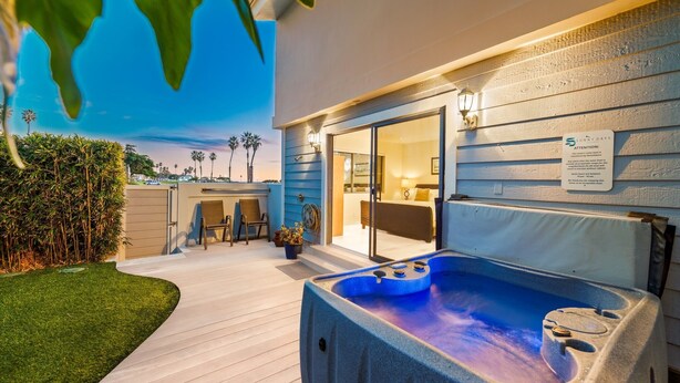 Een modern terras buiten met een hottub, een houten terras en een glazen deur naar een kamer.
