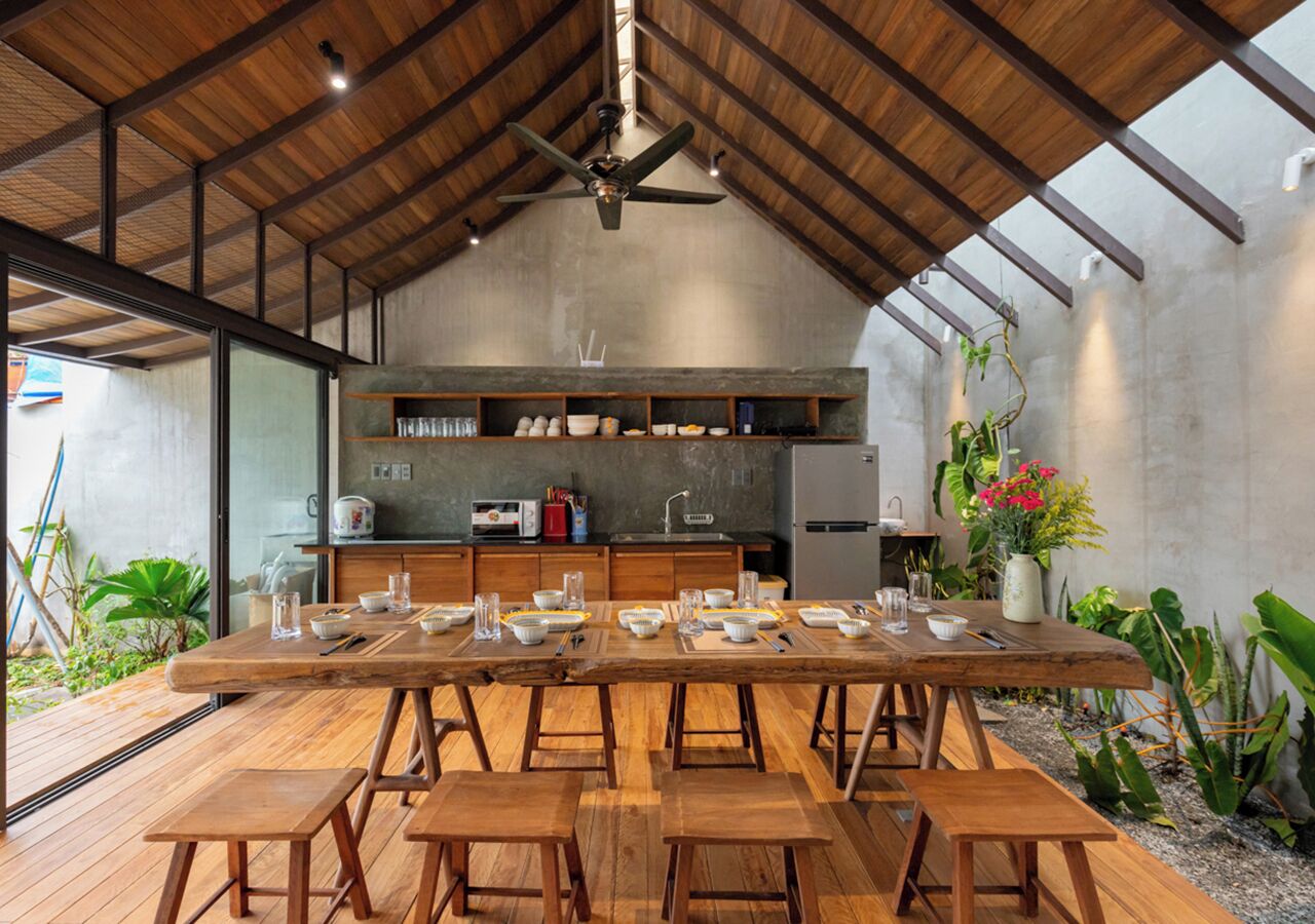 A modern kitchen with a large dining table set for six, wooden stools, and a ceiling fan.