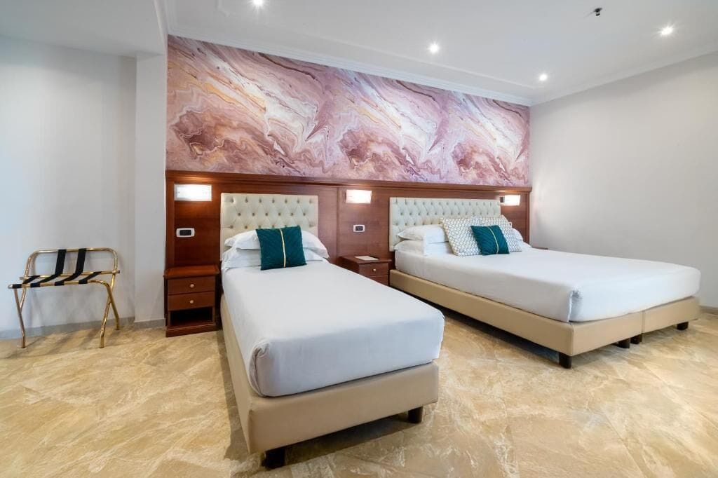 A hotel room with two beds, marble-patterned headboards, a bench, and a marble floor.