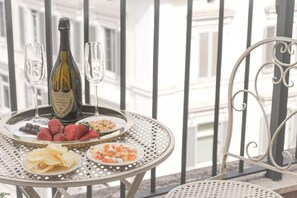 Una mesa metálica redonda con una botella de champán, dos copas y platos de fresas y aperitivos en un balcón.