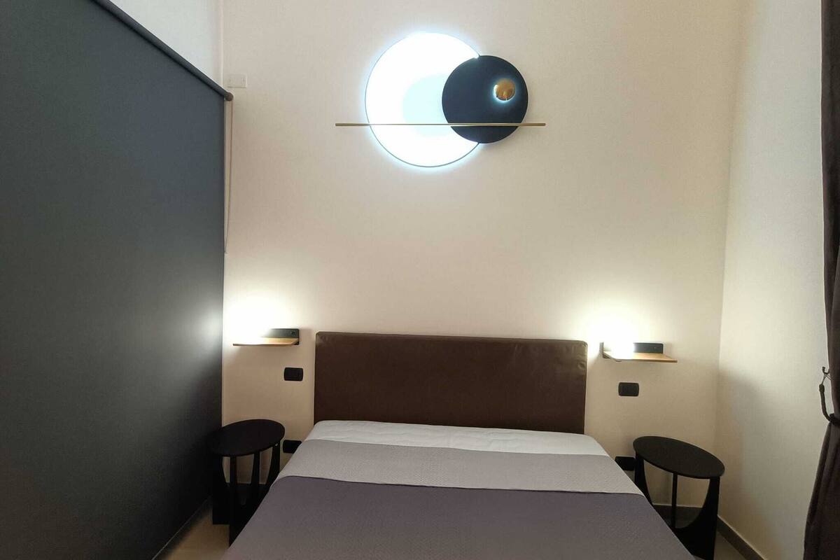 A modern hotel room with a large bed, two bedside tables, and a unique circular wall light fixture.