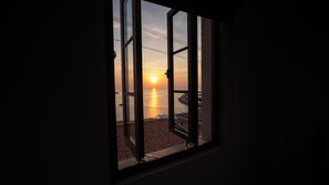 Une fenêtre donnant sur le coucher de soleil sur la mer, un sol carrelé et une rambarde en métal.
