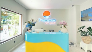 A reception desk with a logo, a reception area, a window with a view, and a potted plant.