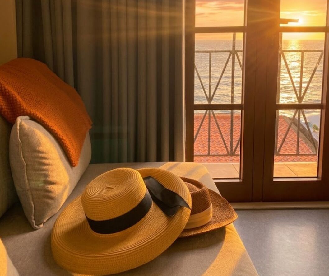 A room with a view of the sea through a window with a metal railing.
