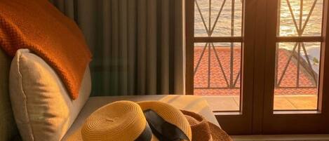 A room with a view of the sea through a window with a metal railing.