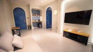 A modern living room with a sofa, a TV, and a kitchen area with blue doors.