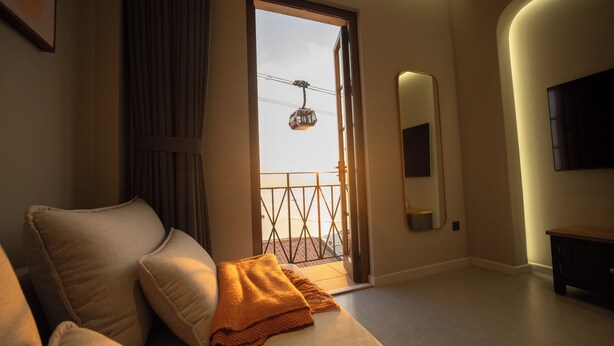 A hotel room with a sofa, a blanket, a mirror, and a TV.