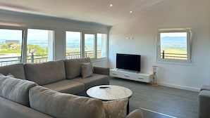 A modern living room with a grey sofa, a round coffee table, a flat-screen TV, and large windows offering a view of a cityscape. - Ishëm Greenview Apartments (Ishëm)