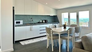 A modern kitchen with white cabinets, a marble countertop, and a dining area with a white table and chairs. - Ishëm Greenview Apartments (Ishëm)