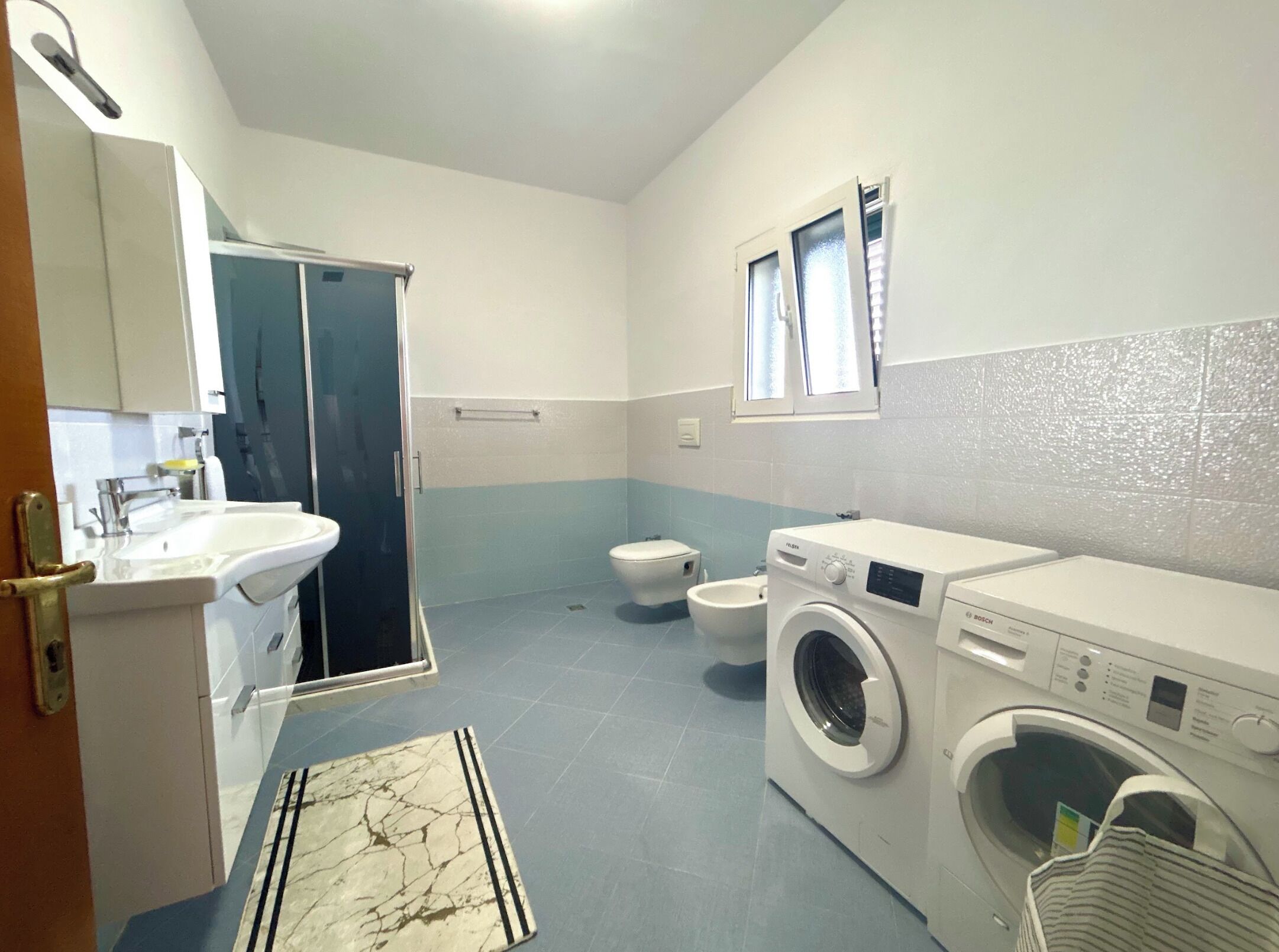 A bathroom with a sink, toilet, shower, and a Bosch washing machine.