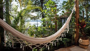 Un hamac dans un jardin luxuriant, parsemé de différentes plantes, avec vue sur la mer.