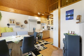 A cozy living room with a dining area, kitchen, and a loft bedroom with a wooden ceiling.