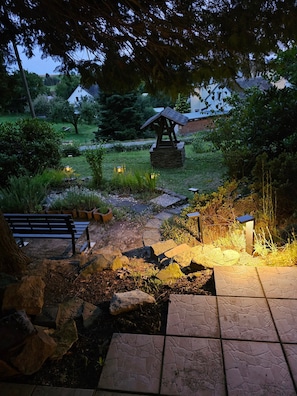 A garden pathway leading to a gazebo, surrounded by greenery and stone tiles.