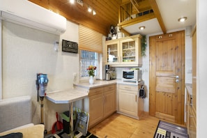 A compact kitchen with wooden cabinets, a microwave, and a small window with blinds.
