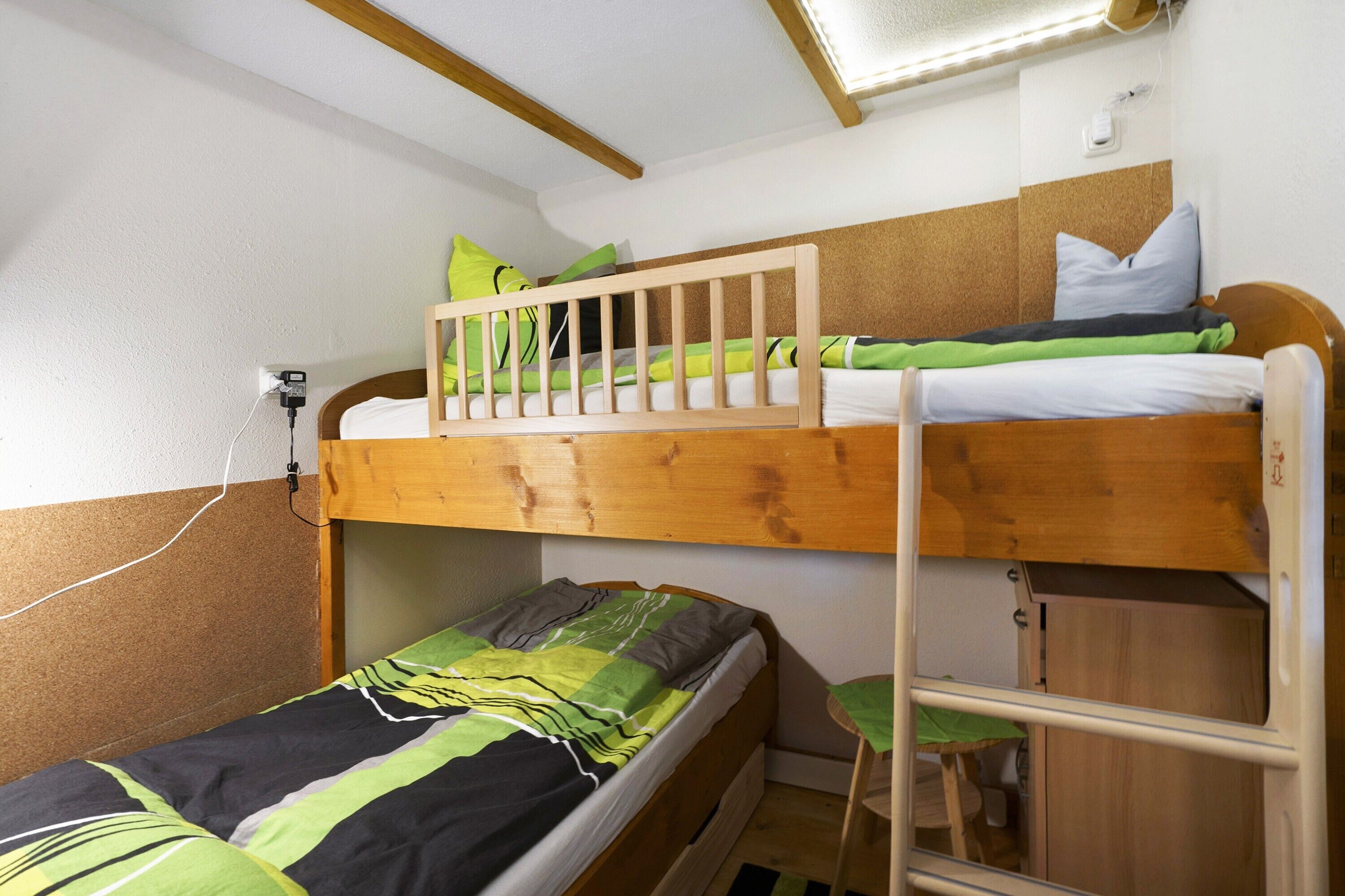 A bunk bed room with a desk and chair, a power outlet, and a window with a light fixture.
