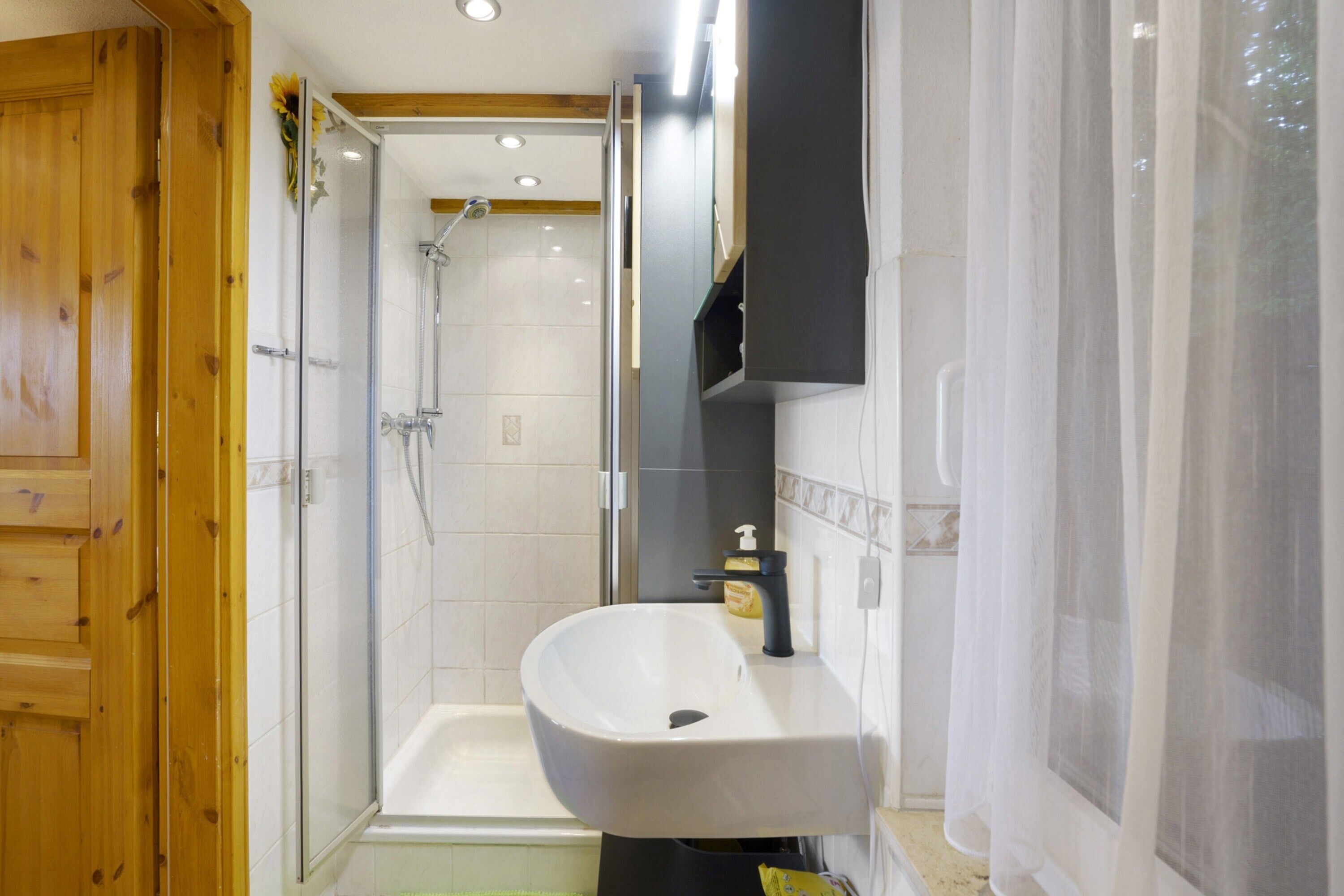 A bathroom with a white sink, a shower, and a wooden door.