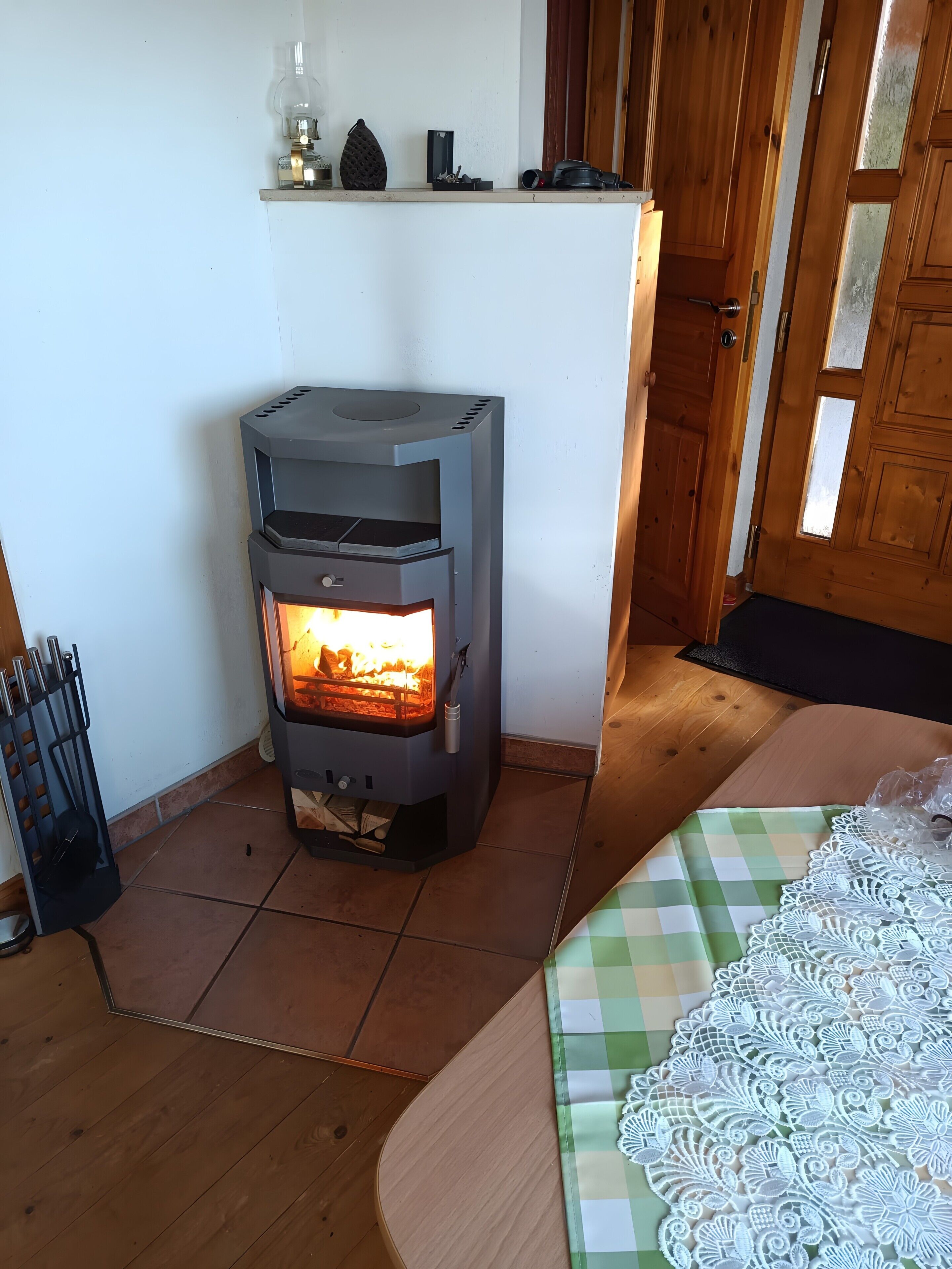 A room with a wood-burning stove, a wooden door, and a checkered tablecloth.