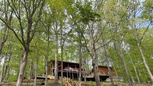 A wooden cabin with a staircase leading to a deck, surrounded by trees.