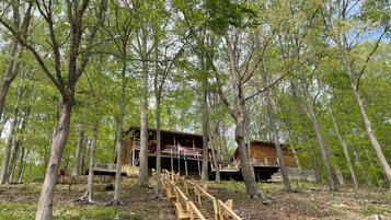 A wooden cabin with a staircase leading to a deck, surrounded by trees.