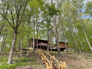 A wooden cabin with a staircase leading to a deck, surrounded by trees.